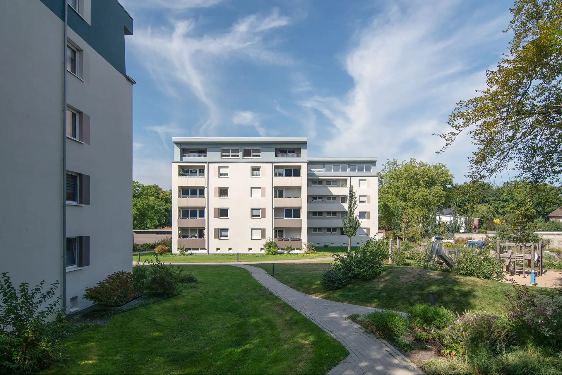 Wohnquartier nach Sanierung und Aufstockung mit weißen Mehrfamilienhäusern und Grünanlage