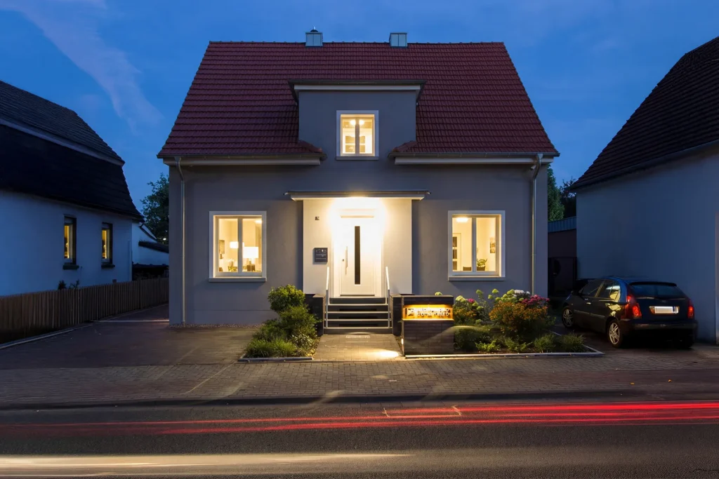 Saniertes Einfamilienhaus mit beleuchtetem Eingang in der Abenddämmerung – Altbausanierung und Umnutzung