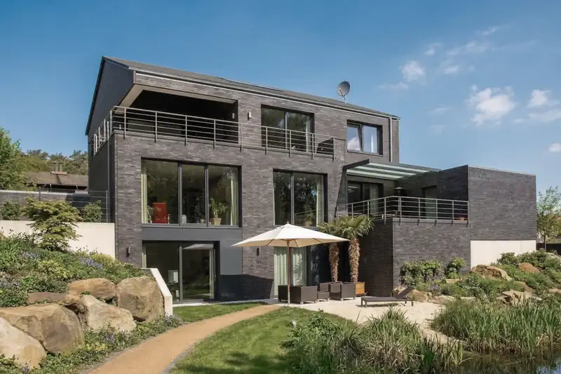 Mit KI optimiertes Foto desselben Mehrfamilienhauses mit dunkler Klinkerfassade und blauem Himmel
